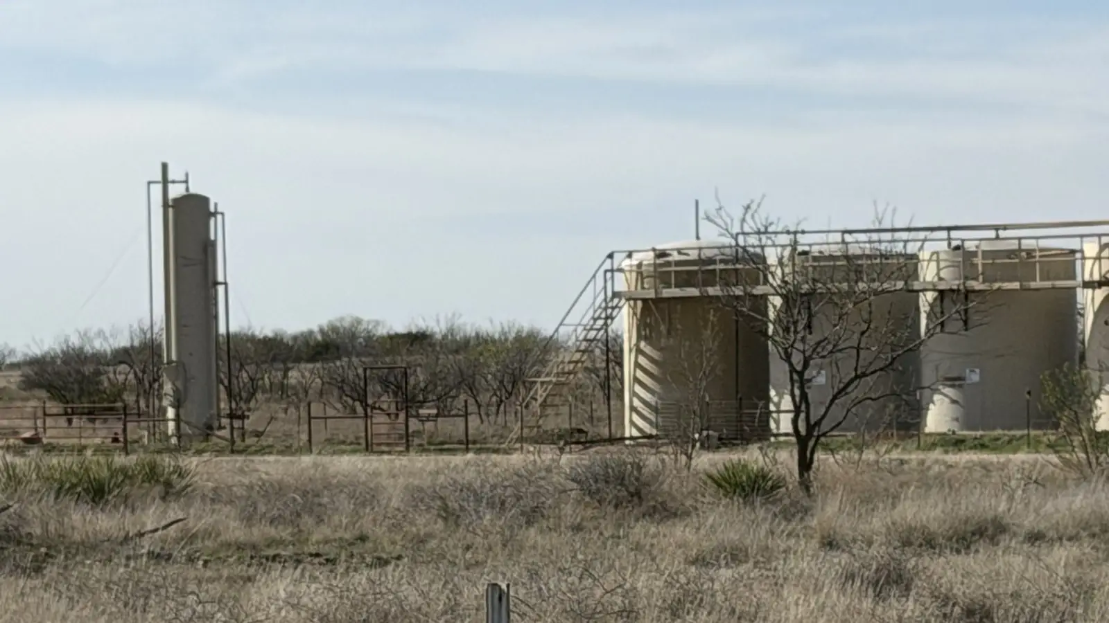 A tank battery of stock tanks with a stair and walkway on a producing property in the United States, open sky behind