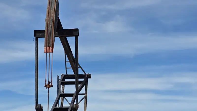 A beam pumping unit in operation on open ground, seen three quarters on against a wide sky