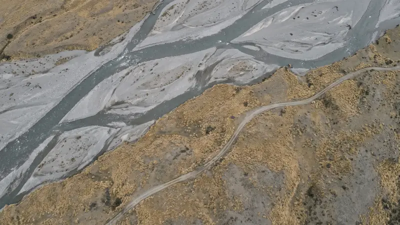 An aerial view looking straight down on a braided gravel river and the surrounding tussock ranges