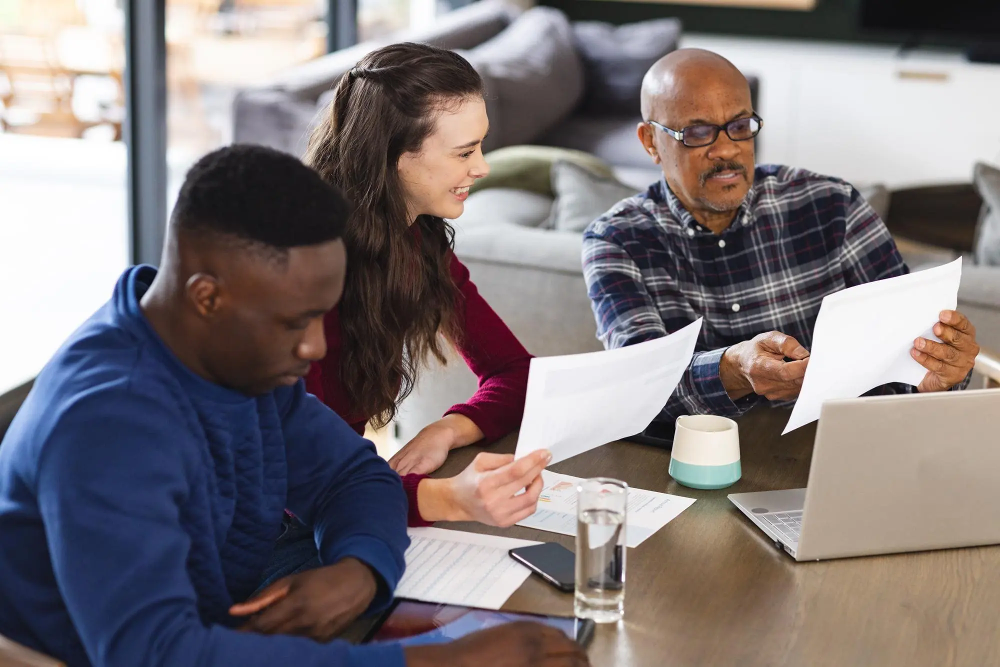 Diverse couple and biracial male financial advisor using laptop and discussing documents at home