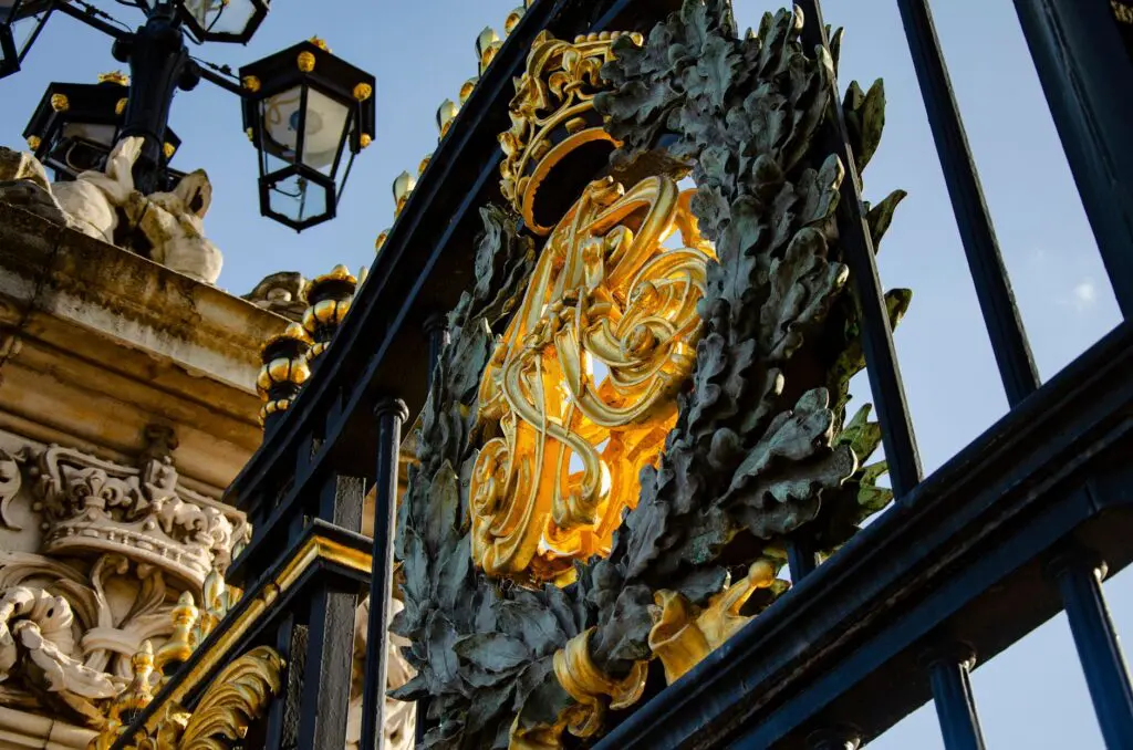 Close-up of gilded ironwork at Buckingham Palace gates in London, showcasing intricate design.