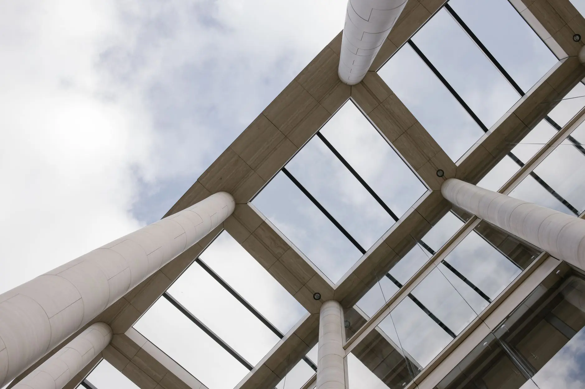Upward view of modern architecture with tall concrete pillars and glass ceilings.